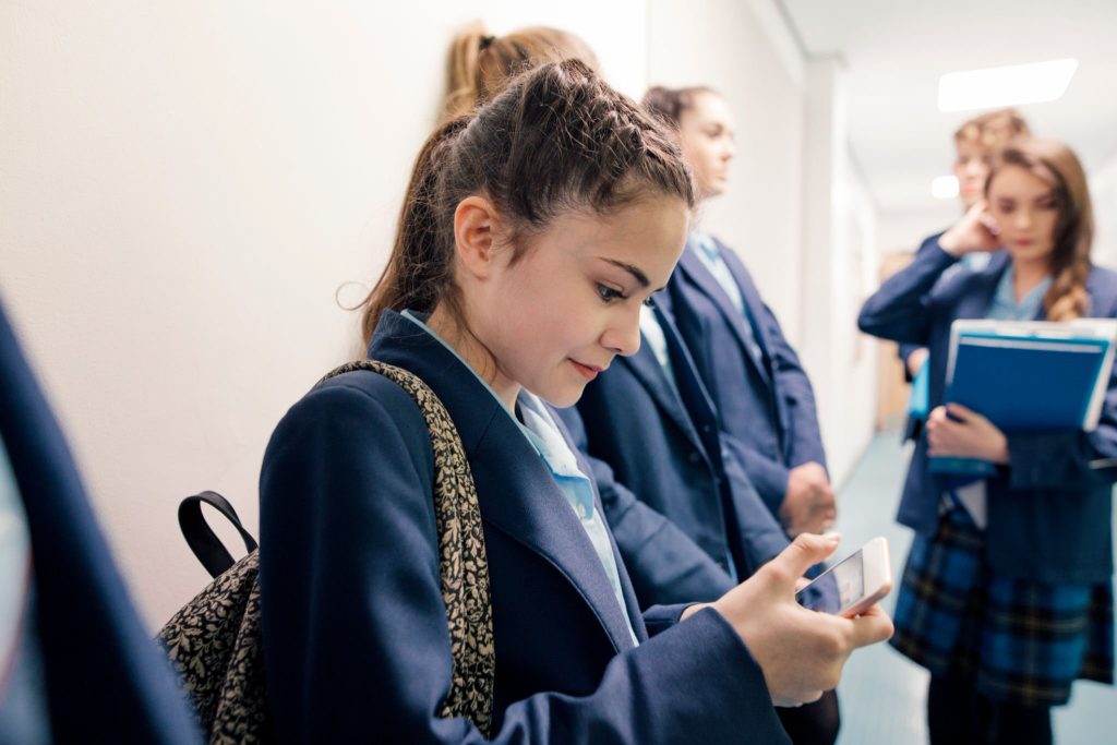 A group of students waiting in line in a school corridor, one is checking her phone