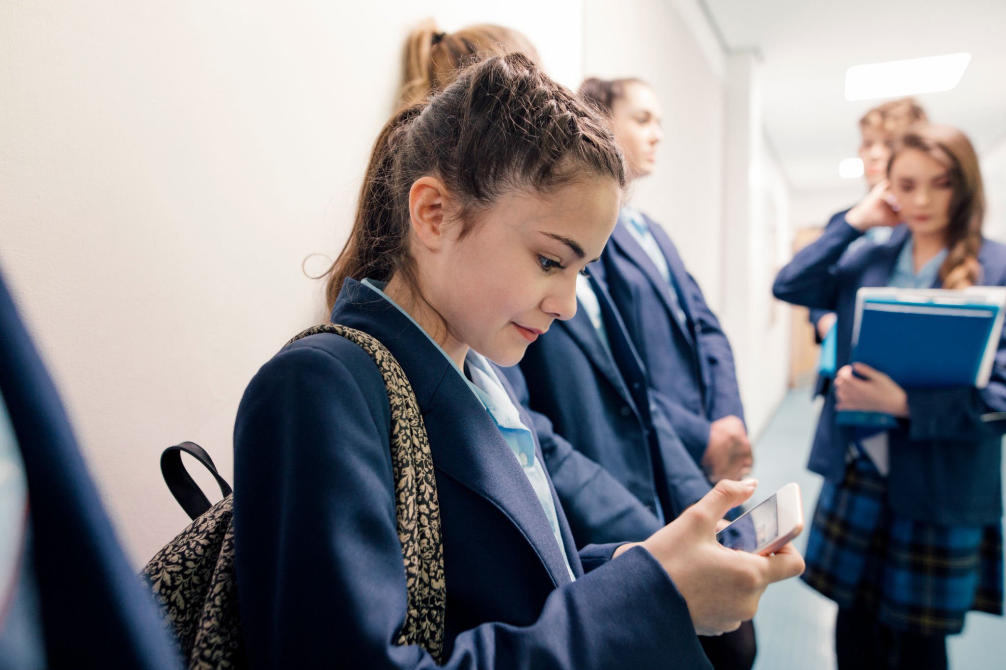 A group of students waiting in line in a school corridor, one is checking her phone
